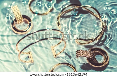 Foto stock: Golden Bracelets Earrings Rings Jewelery On Emerald Water Bac