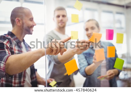 Stockfoto: Businesswoman Holding Adhesive Notes On Window In Creative Offic