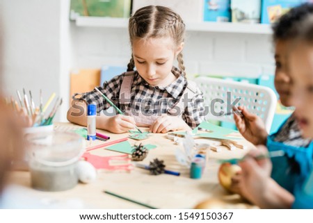 Stock fotó: Young Creative Girl Sitting By Desk Among Classmates And Painting Paper Firtree