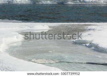 Foto stock: Melting Riverbank By A Slowly Streaming River With A Cottage In The Background
