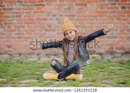 Stock photo: Beautiful Little Girl Sits In Lotus Pose Stretches Arms Wears Yellow Hat Leather Jacket And Rigge