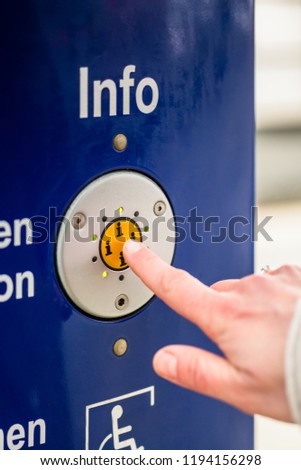 [[stock_photo]]: Woman Pressing Info Button Of Assistance Machine In Train Station