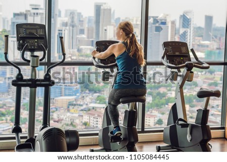 Stockfoto: Young Woman On A Stationary Bike In A Gym On A Big City Background