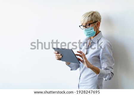 Stock photo: Mature Businesswoman Using A Handheld Tablet And Wear Mask To Pr