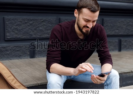 [[stock_photo]]: Handsome Young Guy Sitting On Steps Outdoors Using Mobile Phone Listening Music