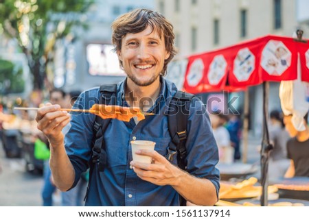 Zdjęcia stock: Young Man Tourist Eating Typical Korean Street Food On A Walking Street Of Seoul Spicy Fast Food Si