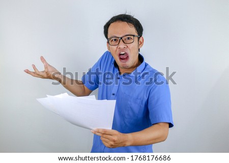 Stock photo: Young Asian Man Is Mad And Angry When Looking On Paper Document Indonesian Man Wearing Blue Shirt