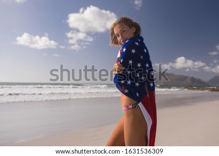 Zdjęcia stock: Side View Of Young Woman Wrapped In American Flag At Beach On A Sunny Day