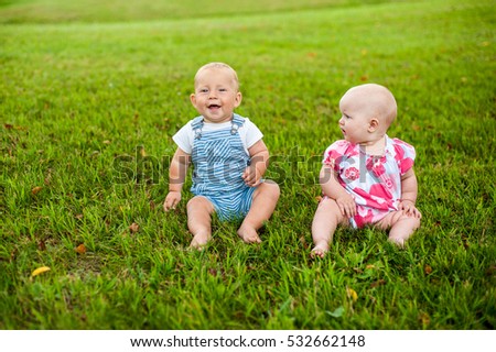 Stock photo: Two Happy Baby Boy And A Girl Age 9 Months Old Sitting On The Grass And Interact Talk Look At Eac