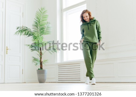 [[stock_photo]]: Full Length Shot Of Cheerful Redhead Slim Female Stands On Tip Toes Near Ballet Barre Has Pilates E