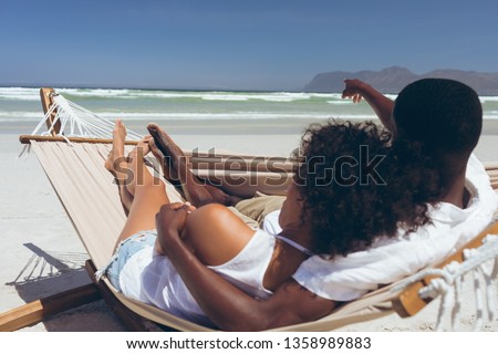 Stock foto: Rear View Of Cute Multi Ethnic Couple Relaxing On Hammock While African American Male Points At Some