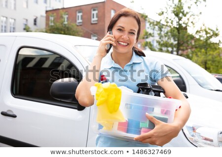 Stockfoto: Smiling Janitor Holding Cleansing Product Talking On Smartphone