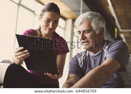 ストックフォト: Happy Young Female Trainer Assisting Senior Man In Fitness Studio