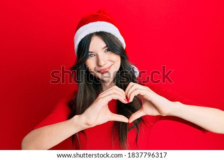 Foto d'archivio: Young Beautiful Woman Wearing Christmas Hat Showing Heart Shape