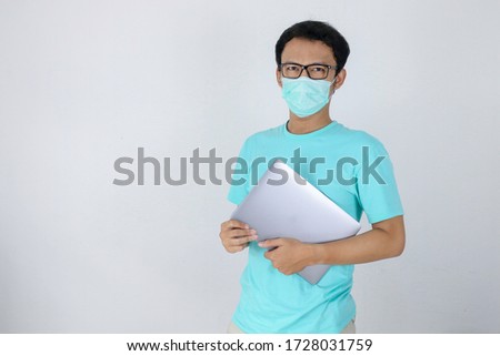 Stok fotoğraf: Young Asian Man Wear Medical Mask Is Carrying A Laptop Indonesian Man Wearing Blue Shirt
