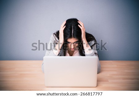 Stockfoto: Tired Young Woman Sitting At The Table Isolated Over Grey Background Near Laptop Computer