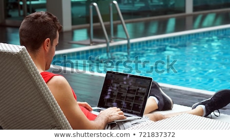 Stock photo: Young Man Looking At His Laptop By The Pool