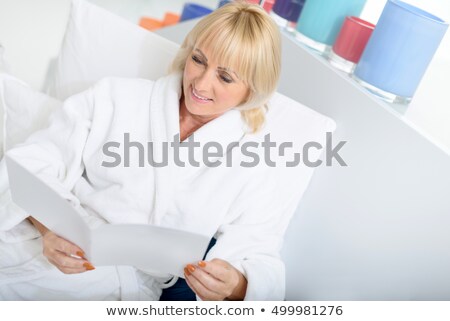 Foto stock: Cute Lovely Serene Female Sitting At Home And Reading Magazine
