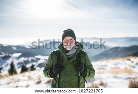 Stockfoto: Front View Of Active Senior Man Looking At Camera Standing At The Beach With Mountains In The Backgr