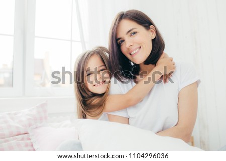 Foto stock: Positive Daughter And Mum Embrace Each Other Being In High Spirit After Good Sleep Pose In Bedroom