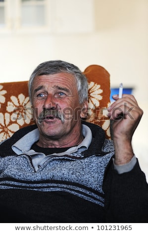 Old Man With Mustache Smoking Cigarette While Sitting In Sofa And Speaking Foto stock © Zurijeta