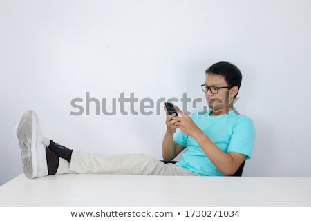 Stock photo: Young Asian Man With Happy Face With What He See On A Mobile Phone With Leg On The Table Indonesian