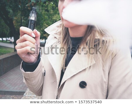 Stok fotoğraf: Blond Girl In Beige Trench Coat Vaping Fruit E Liquid With Very