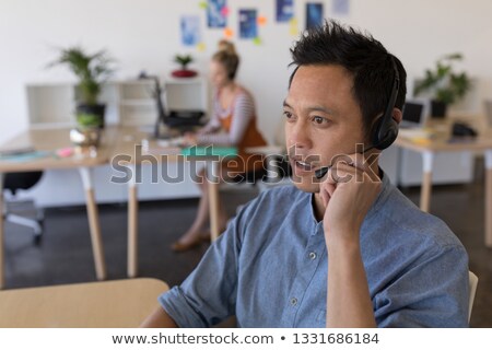Foto stock: Side View Of Asian Male Executive Looking Into Distance While Talking On Headset At Desk In Office