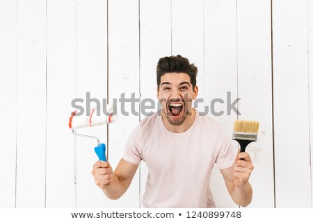 Сток-фото: Portrait Of Excited Man 20s Holding Paint Roller And Brush Whil