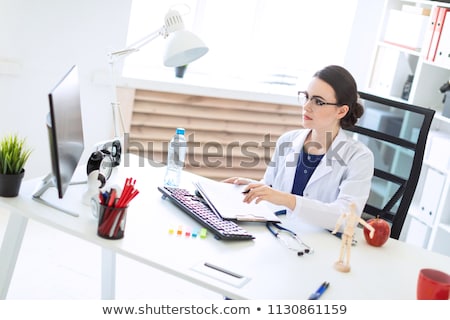 Foto d'archivio: A Beautiful Young Girl In A White Robe Is Sitting At A Computer Desk With Documents And A Pen In Her
