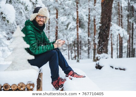 Stockfoto: Photo Of Cheerful Male Types Messages On Smart Phone Looks Directly Into Camera Sits In White Winte