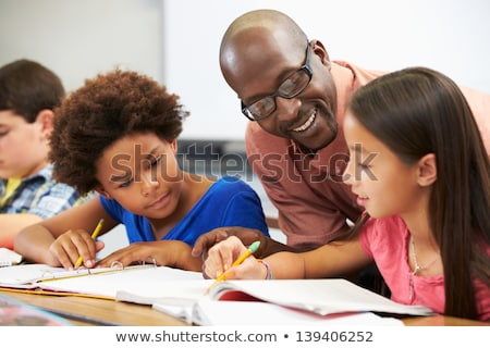 Stok fotoğraf: Teacher Helping Male Pupil Studying At Desk In Classroom