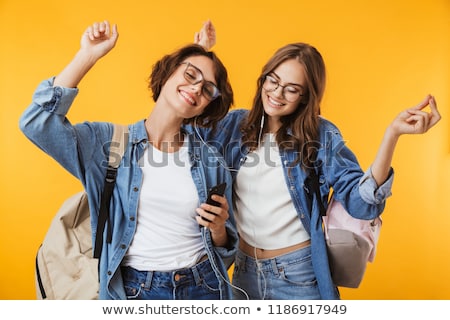 Stockfoto: Women Friends Isolated Over Yellow Wall Background Using Mobile Phone Listening Music With Earphones