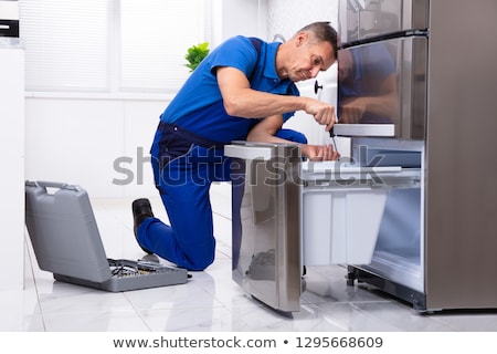 [[stock_photo]]: Repairman Fixing Refrigerator With Screwdriver