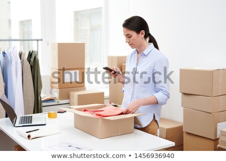 Foto d'archivio: Young Mobile Female With Smartphone Taking Photo Of Folded Pullover In Open Box