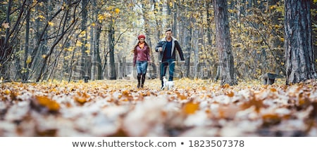 Foto stock: Woman And Man In The Fall Strolling With Their Dog In The Park