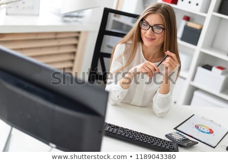 Stock photo: A Young Blonde Girl Sits At A Computer Desk In The Office And Holds A Pencil In Her Hand