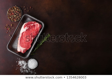 Foto d'archivio: Raw Sirloin Beef Steak In Plastic Tray With Knife And Fork On Rusty Background Salt And Pepper With