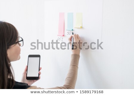 [[stock_photo]]: Young Female Broker Writing Down Percentage Under Paper Chart On Whiteboard