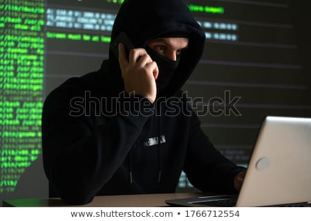 Foto stock: Hacker With Program On Computer Calling On Cell