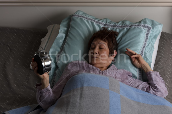 Restless senior woman looking at alarm clock during nighttime wh Stock photo © tab62