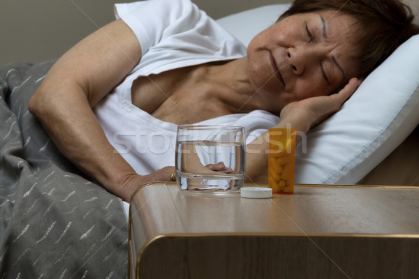 Bottle of medicine and water with senior woman sleeping in backg Stock photo © tab62