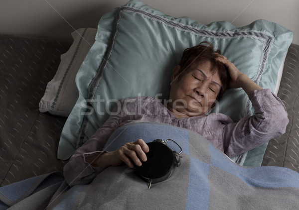 Restless senior woman holding alarm clock upside down during nig Stock photo © tab62
