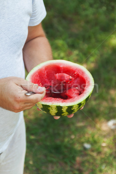 Stock photo: A young man is eating a watermelon with a spoon. The concept of 