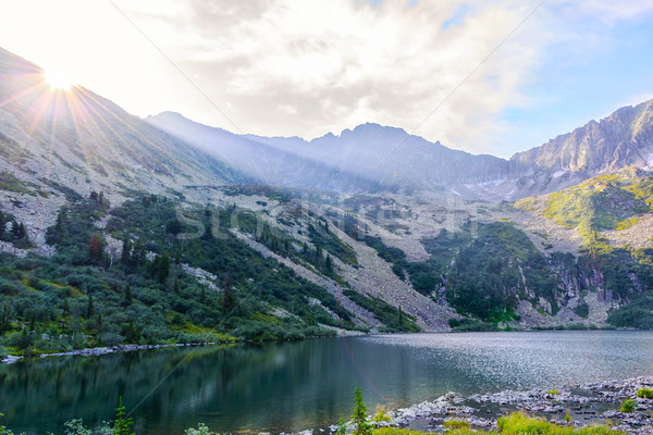 Beautiful lake landscape with sun beams over mountain range  Stock photo © TasiPas