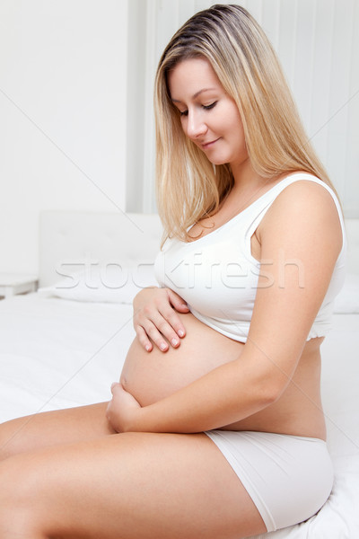 Stock photo: Pregnant woman sitting on bed and looking on belly