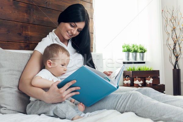 Stock photo: Child education. Happy mother with her toddler sitting on the bed and reading a book