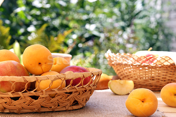 Apricots and apples in wattled basket on sackcloth on a wooden t Stock photo © user_11056481