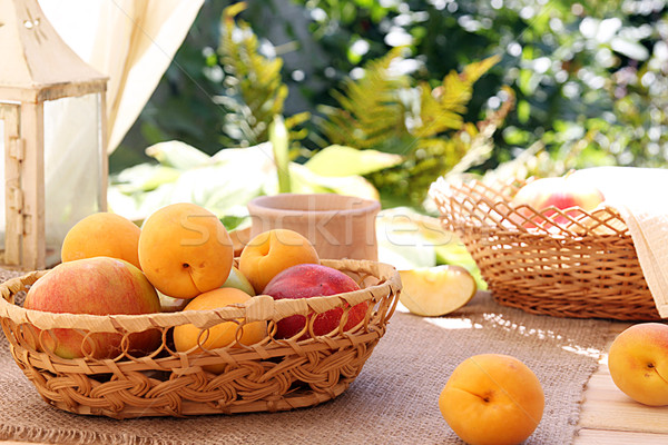 Apricots and apples in wattled basket on sackcloth on a wooden t Stock photo © user_11056481