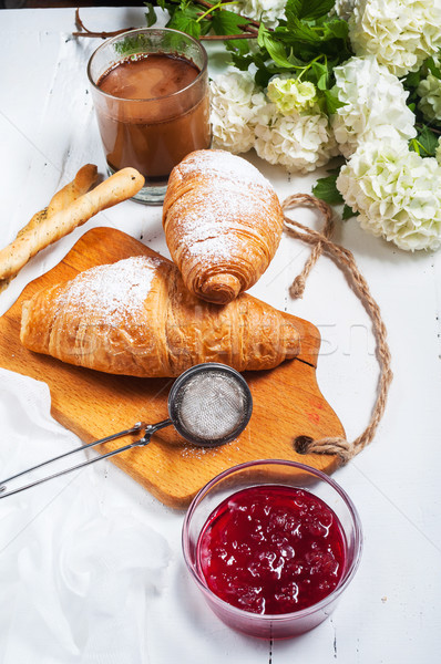 Breakfast with fresh croissants, glass of coffee, milk, strawberry jam and flowers on a white wooden Stock photo © voloshin311